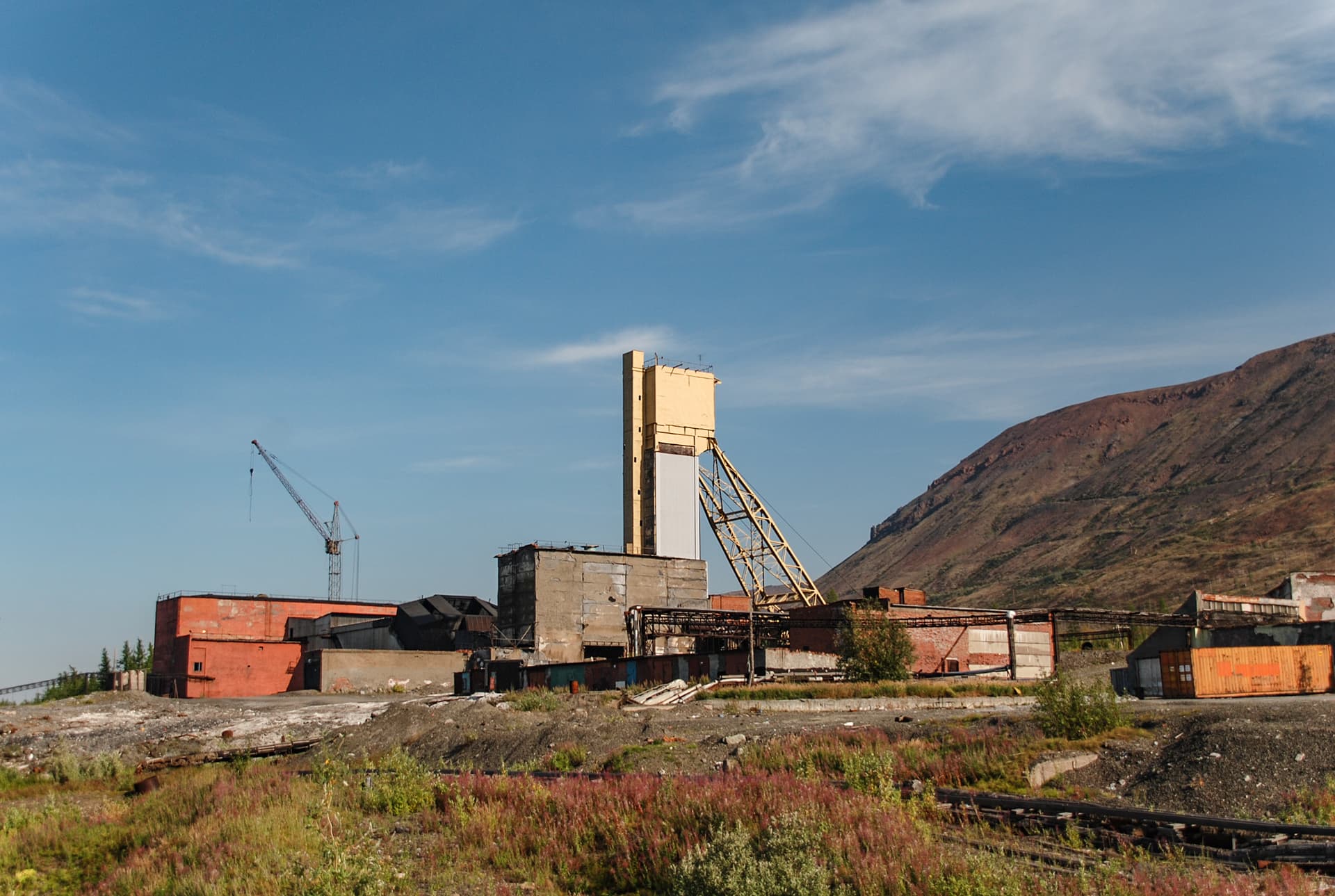 Abandoned copper and nickel mine site in Minnesota, with derelict headframe, crane and outbuildings against a ridge